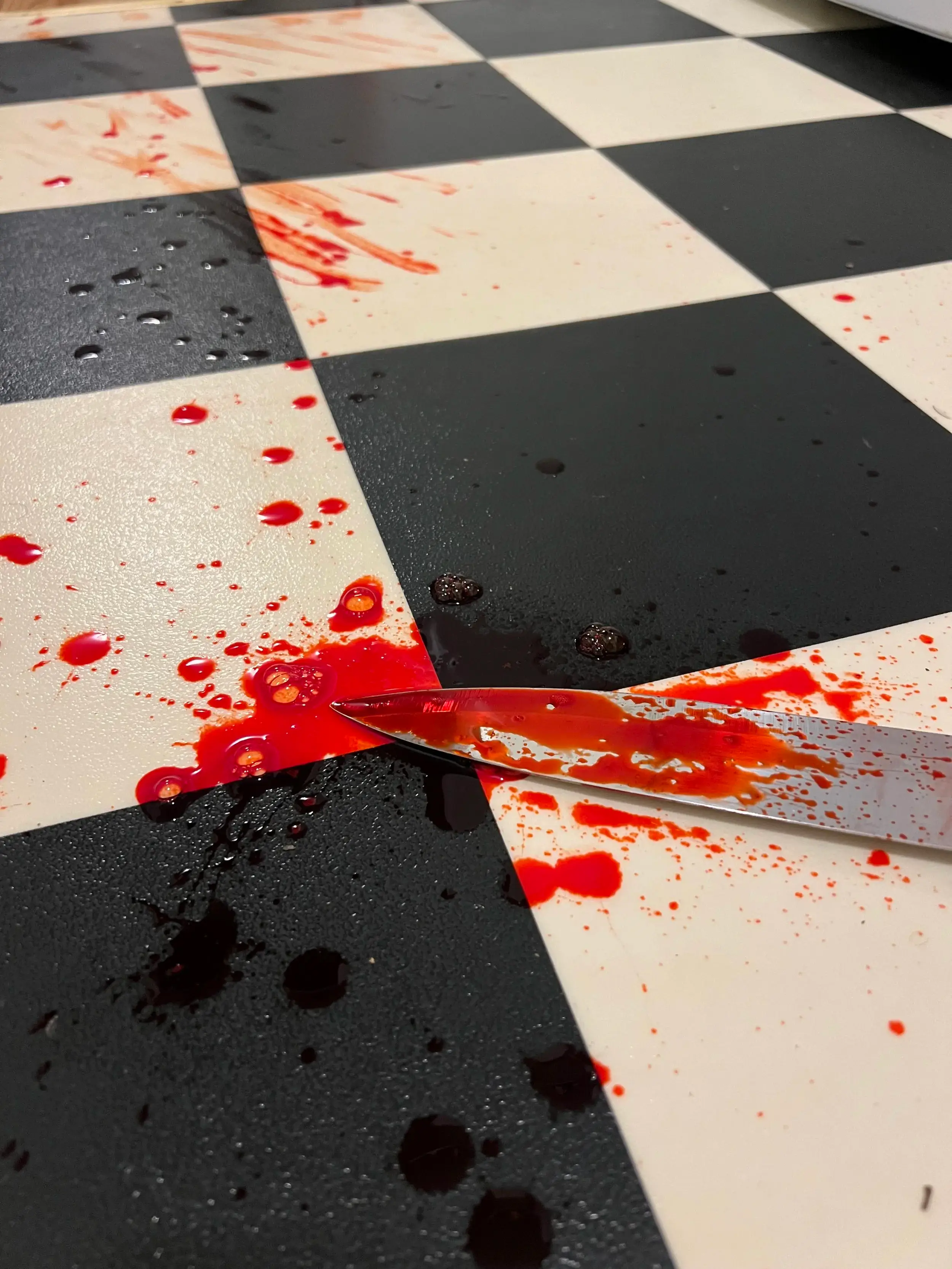 Bloodied kitchen knife on a checkerboard floor with blood spatter