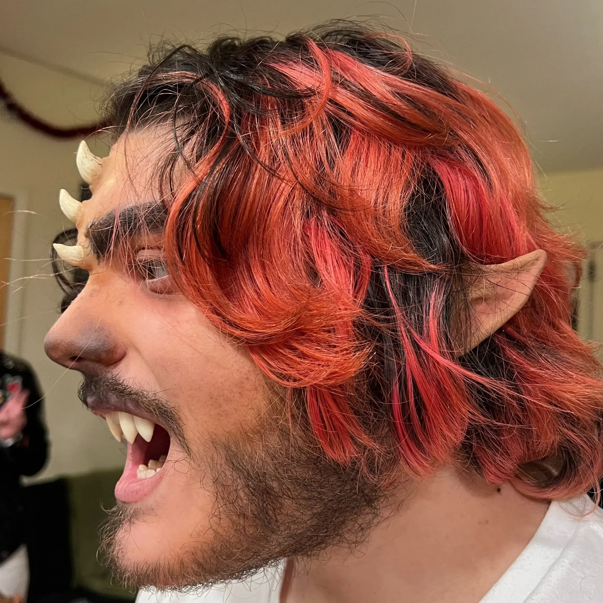 Faun in profile with horns, pointed prosthetic ear, fangs and red-streaked hair
