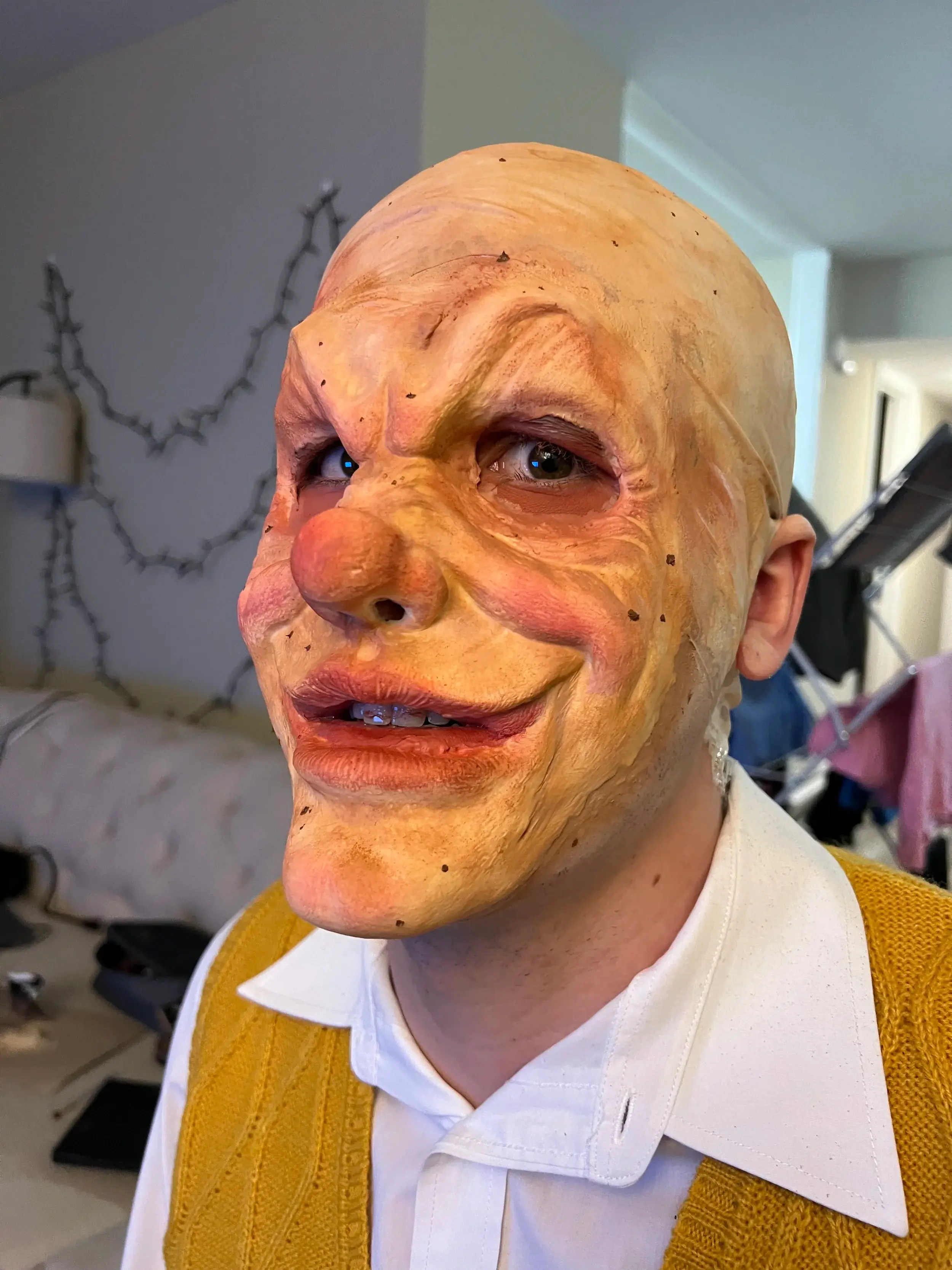 Full-face foam latex prosthetic of a bald, grinning old man with a hooked nose, worn with a collar and waistcoat