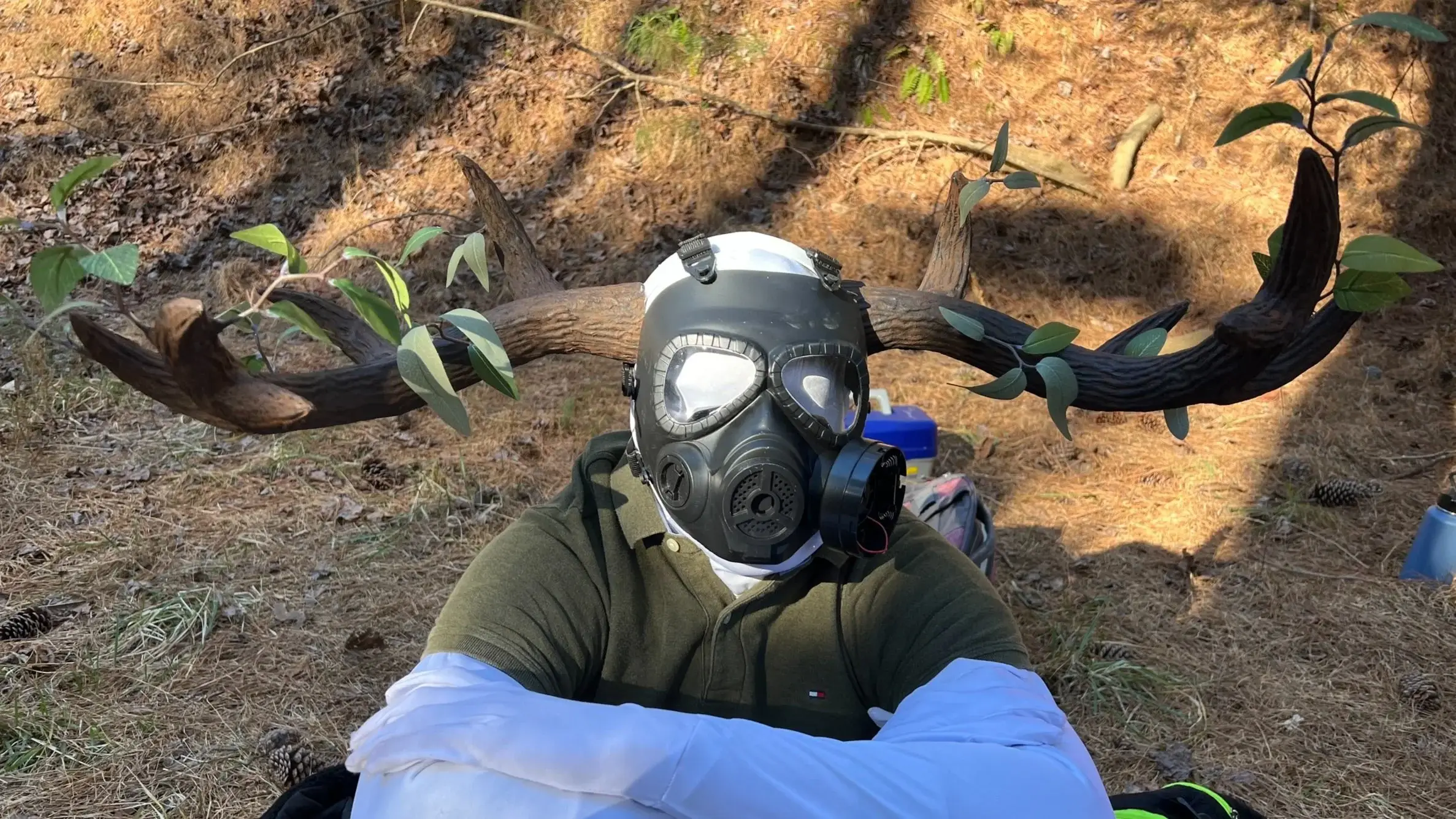 Figure in a gas mask lying on a forest floor with long clawed arms outstretched