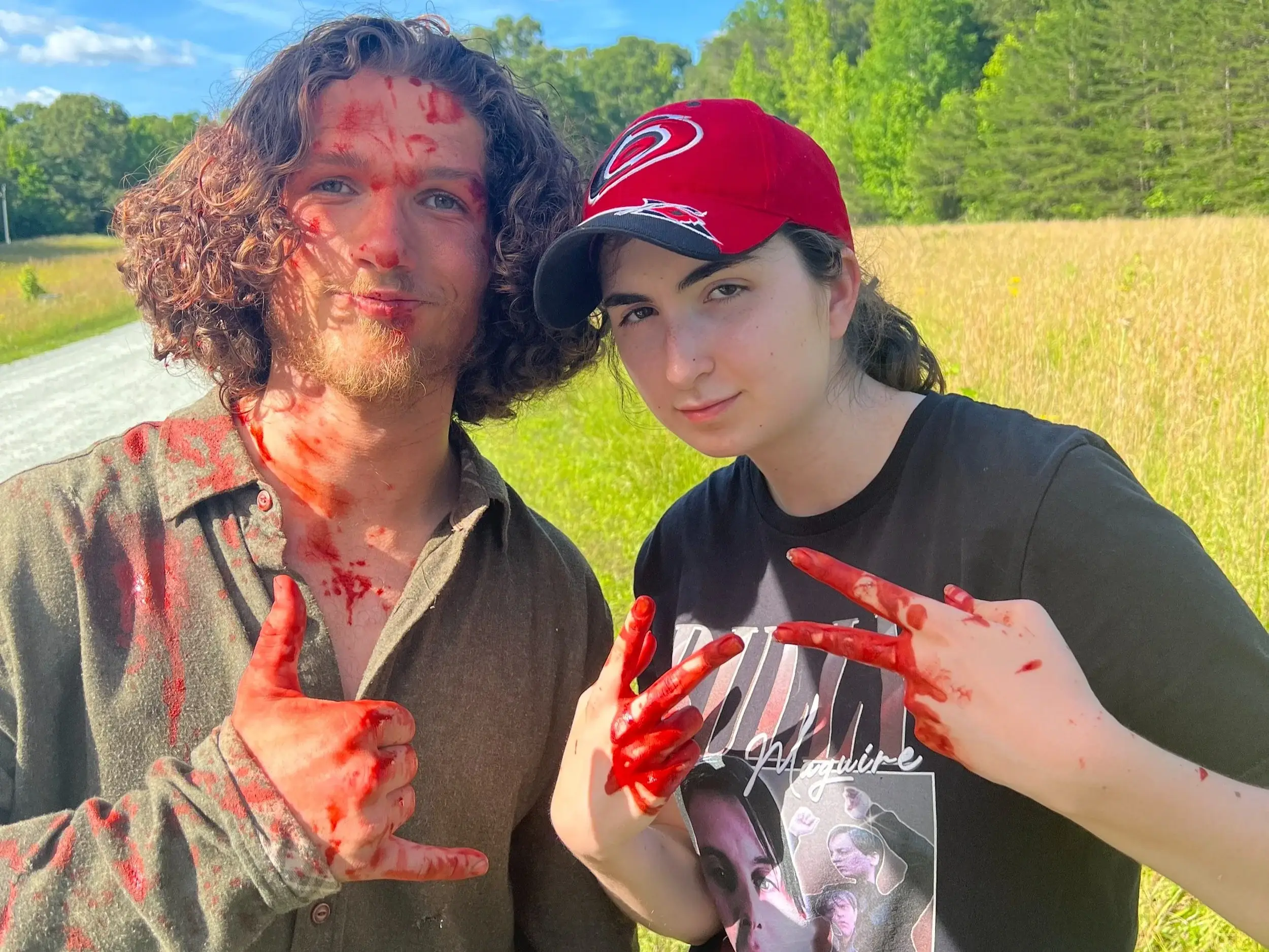 Two people on location in a field, both holding up blood-covered hands