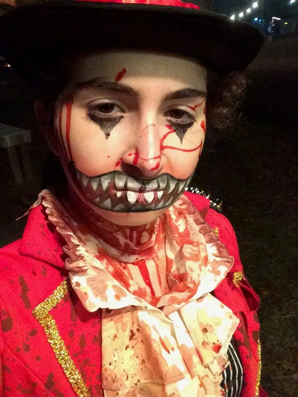 Clown with a stitched-on grin of jagged teeth in a blood-soaked ringmaster coat